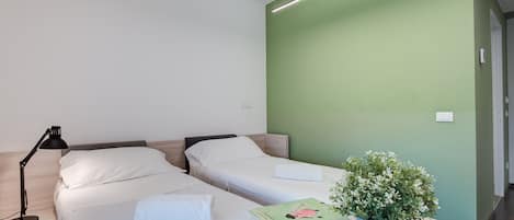 A hotel room with two beds, a desk with a lamp, and a potted plant.