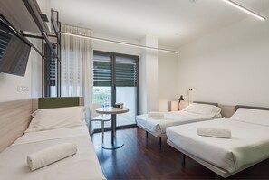A modern hotel room with two single beds, a small table, and a chair.