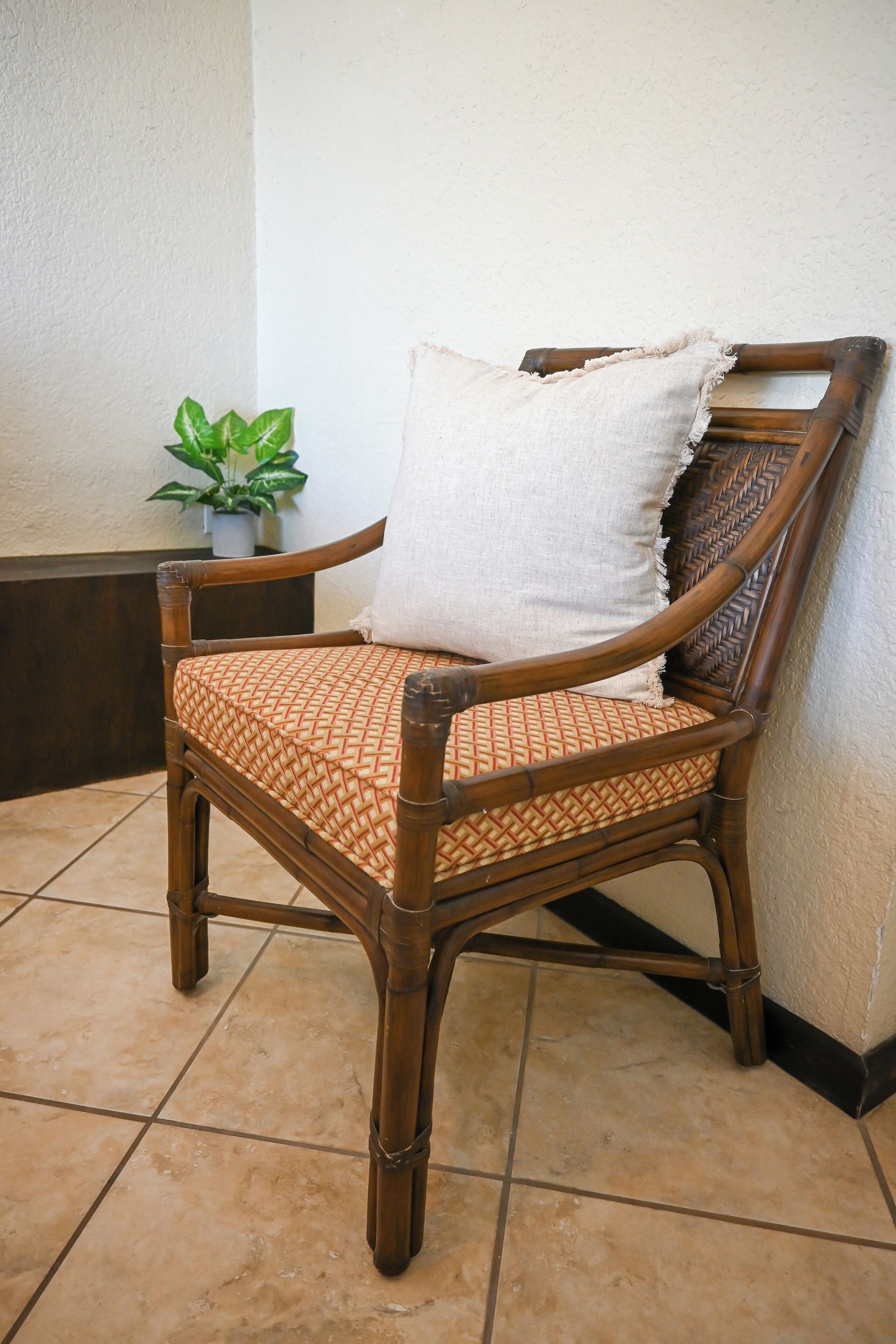 A wooden chair with a woven cushion and a white pillow, placed against a wall with a potted plant nearby.