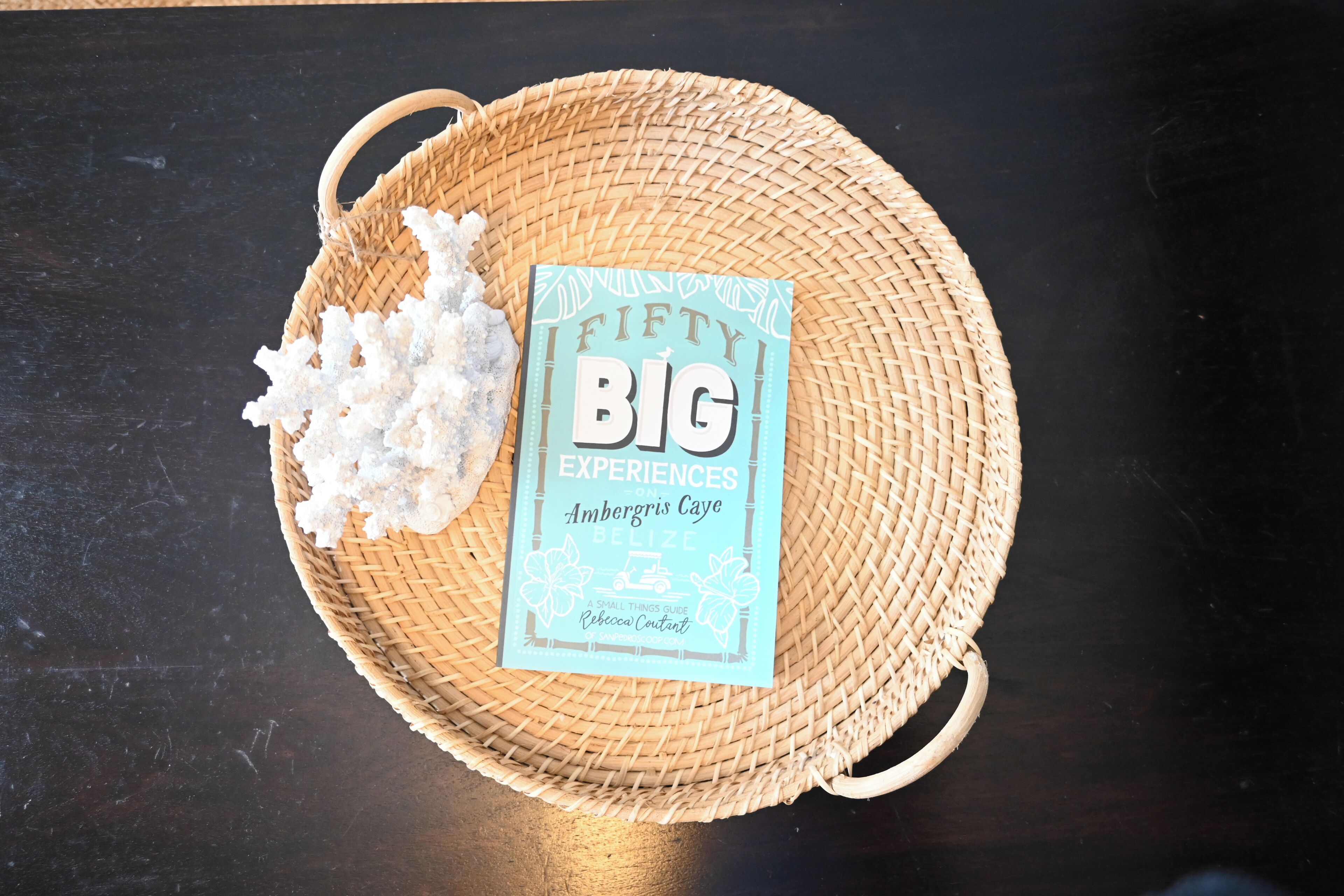 A woven basket containing a book titled "Fifty Big Experiences" and some white crystals on a dark surface.