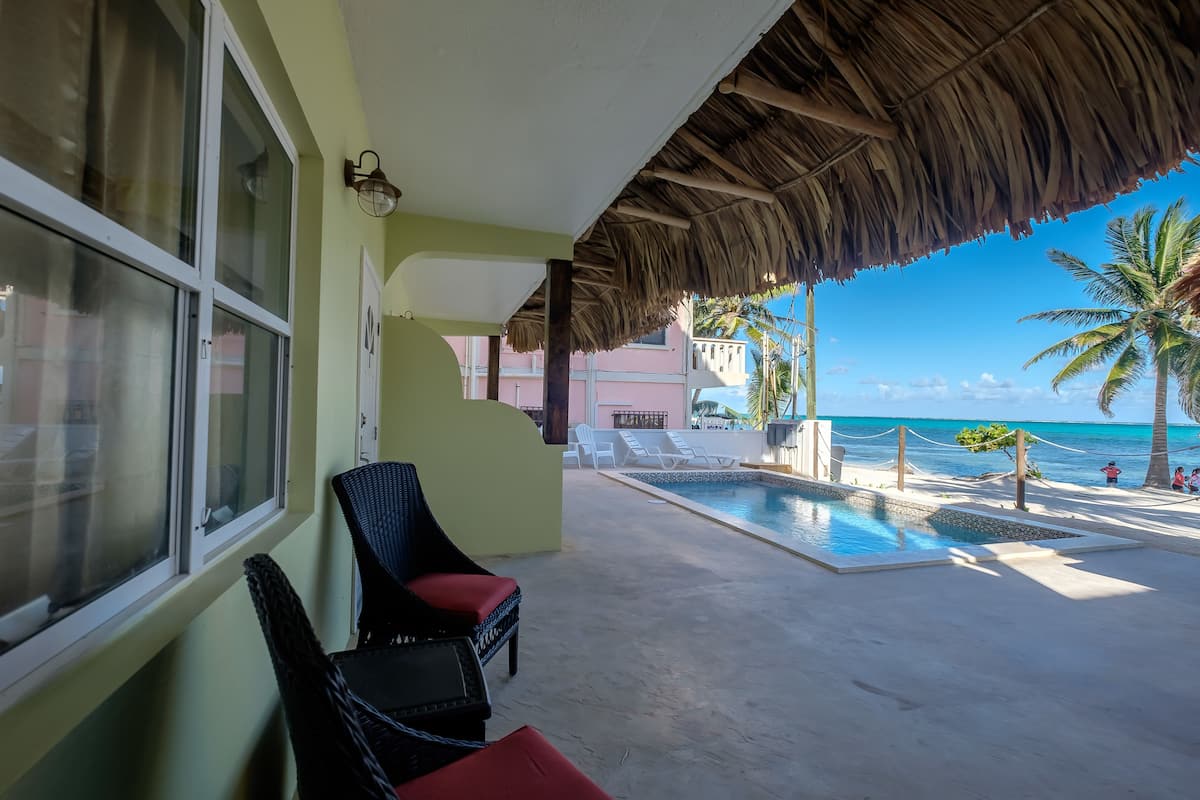 Zona junto a la piscina con sillones de descanso, techo de paja y vista al océano.