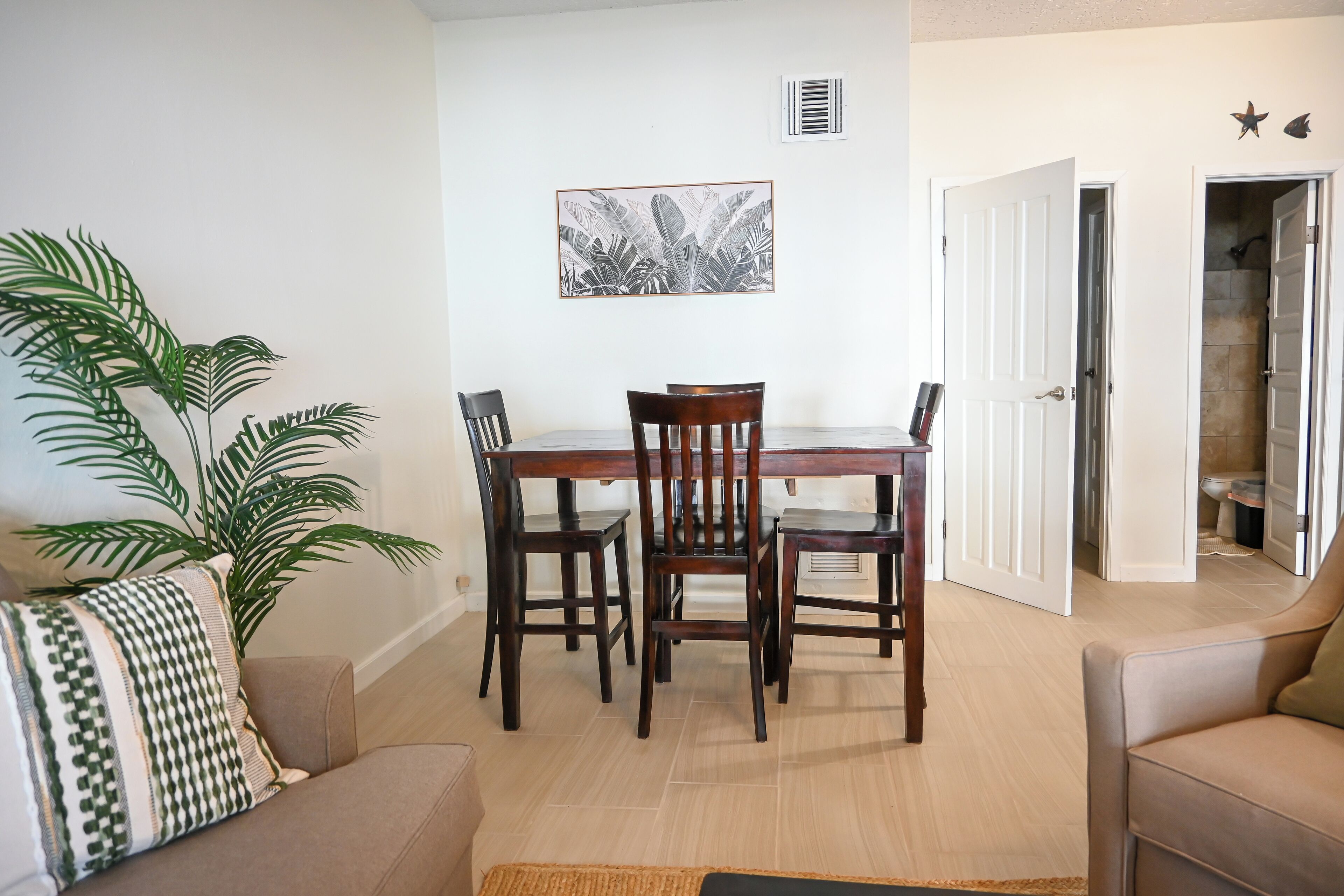 Un comedor con una mesa y sillas de madera, una planta en maceta y un cuadro en la pared.