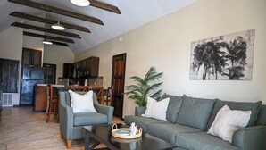 Una sala de estar moderna con sofá, sillas, una mesa de centro y una zona de comedor con una cocina al fondo.