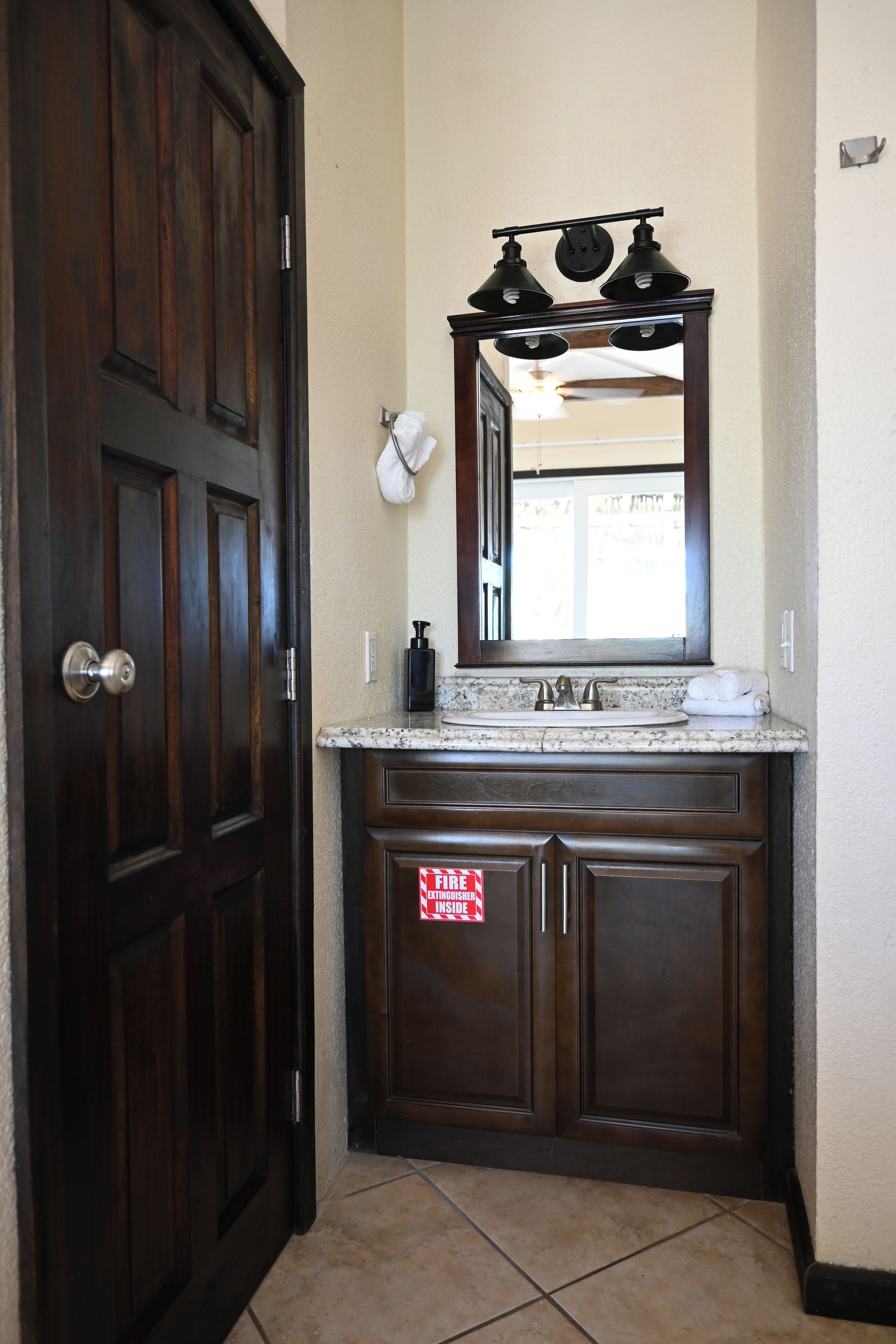 A bathroom with a dark wooden door, a marble countertop, a sink, and a mirror above it.