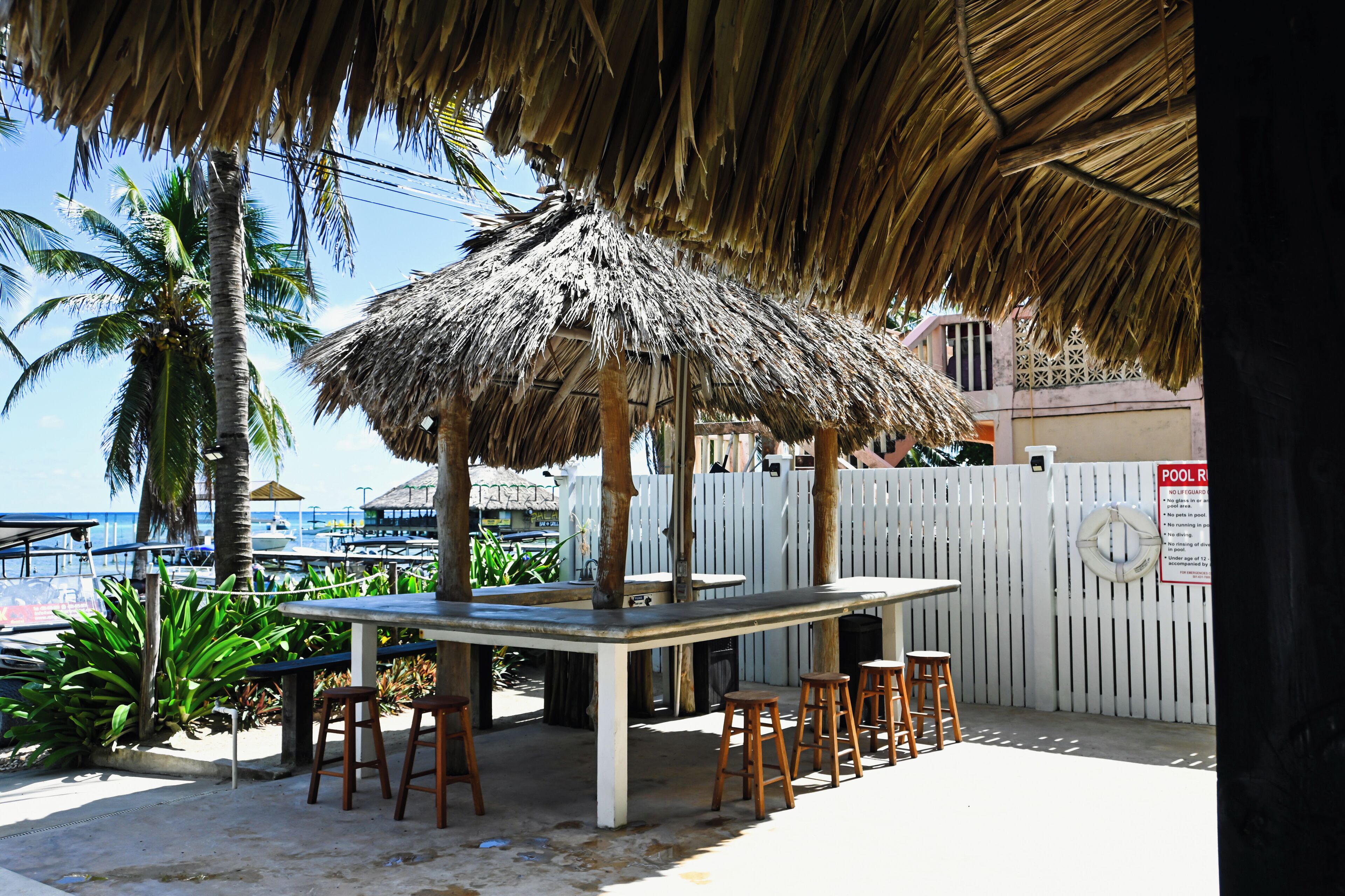 A beachside bar with a thatched roof, wooden stools, and a view of the sea.