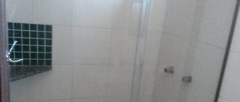 A glass-enclosed shower stall with white tiles, a metal door, and a small shelf with a green object.