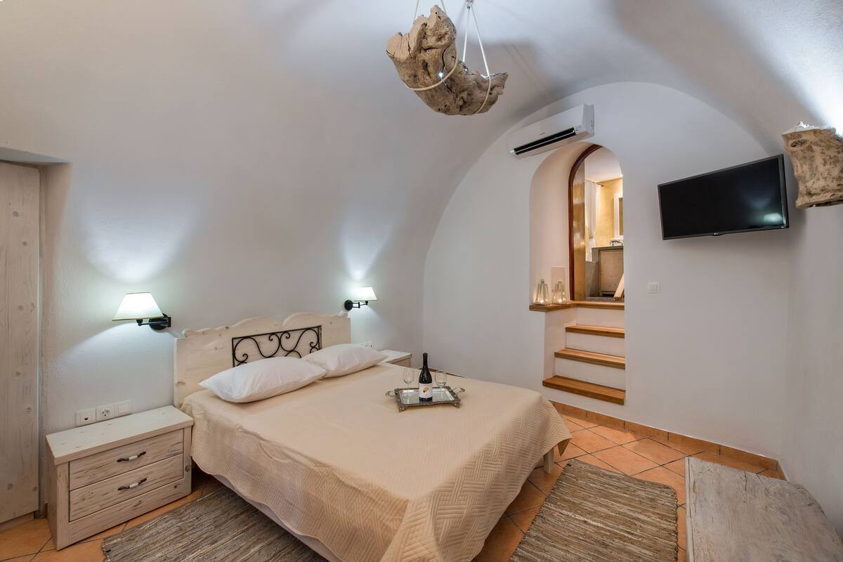 A bedroom with a bed, bedside lamps, a TV, a wooden nightstand, and a unique ceiling light fixture.