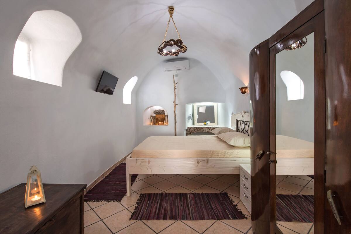 A bedroom with a wooden bed, a dark wooden dresser, a mirror, and a hanging light fixture.