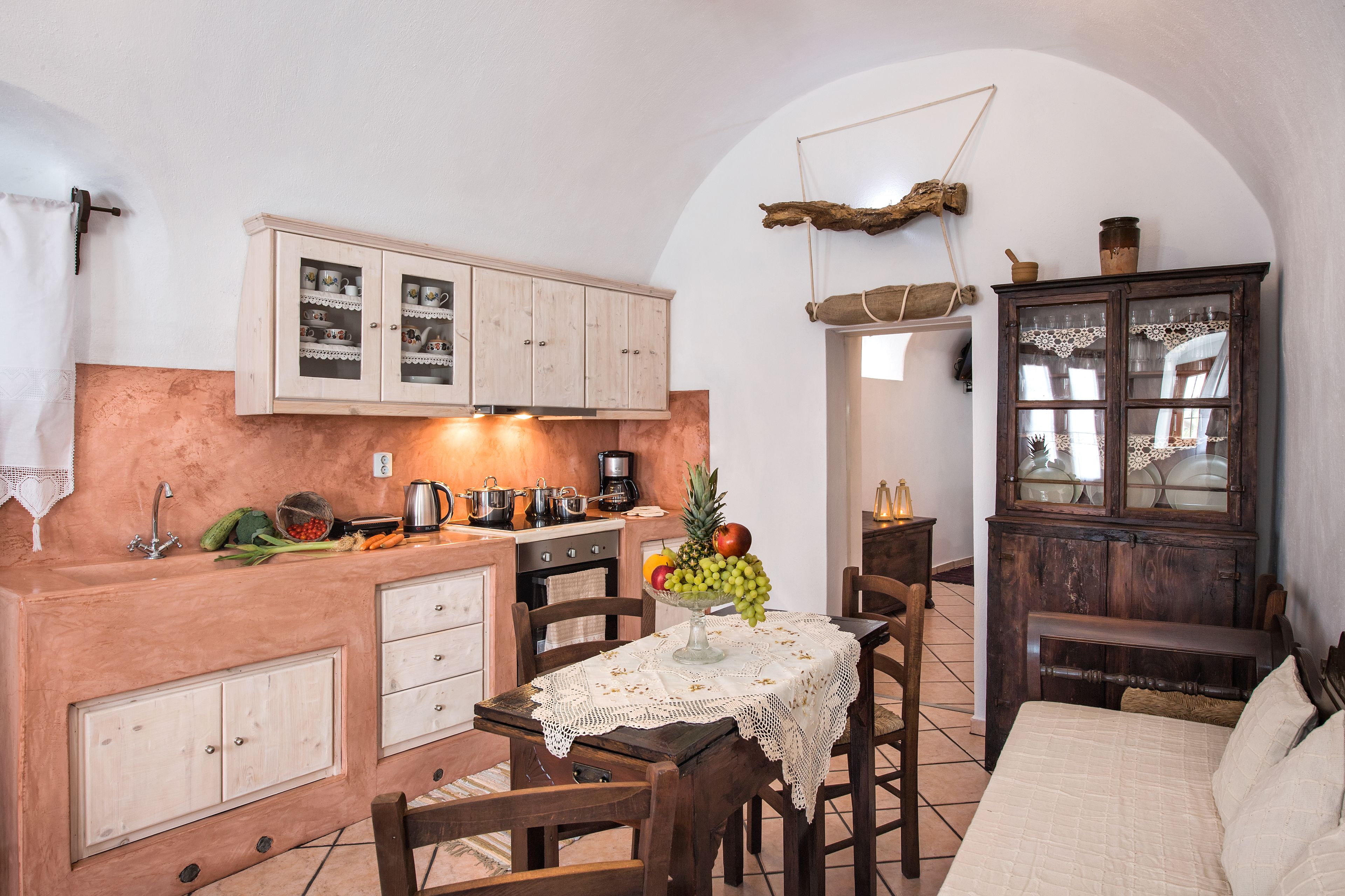 A cozy kitchen with wooden cabinets, a dining table with a lace tablecloth, and a fruit bowl.