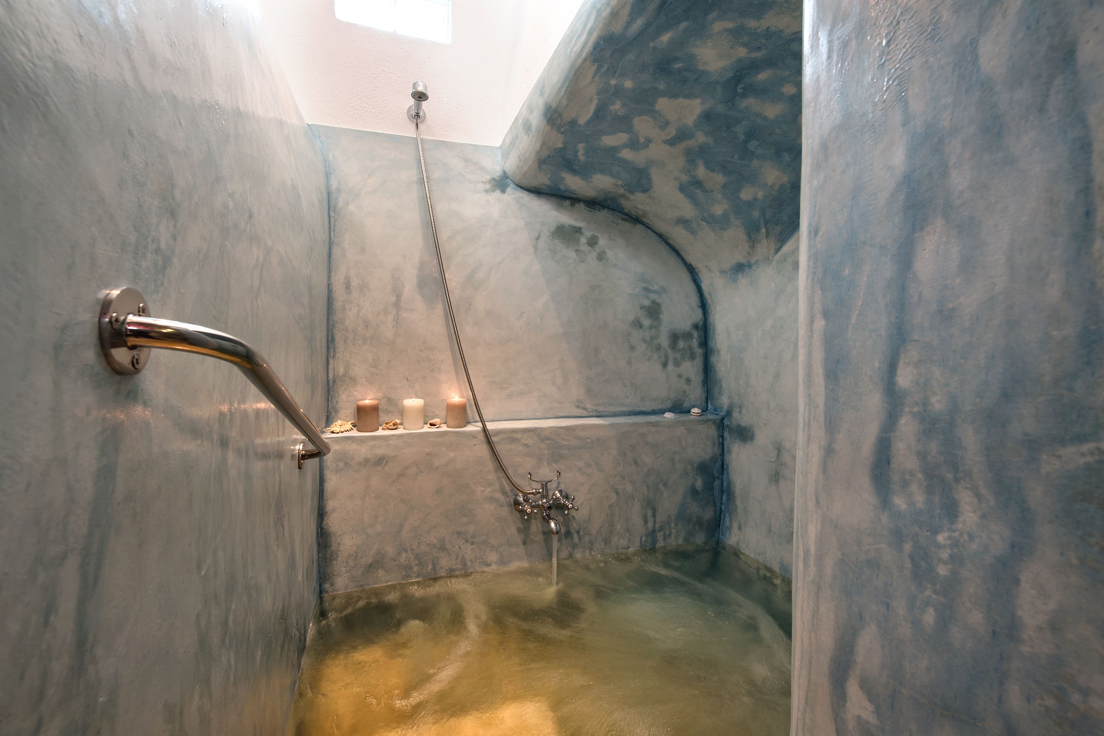 Un baño con bañera, ducha y ducha de mano. Hay velas en un estante sobre la bañera.