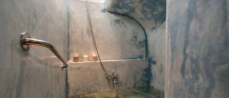 Un baño con bañera, ducha y ducha de mano. Hay velas en un estante sobre la bañera.