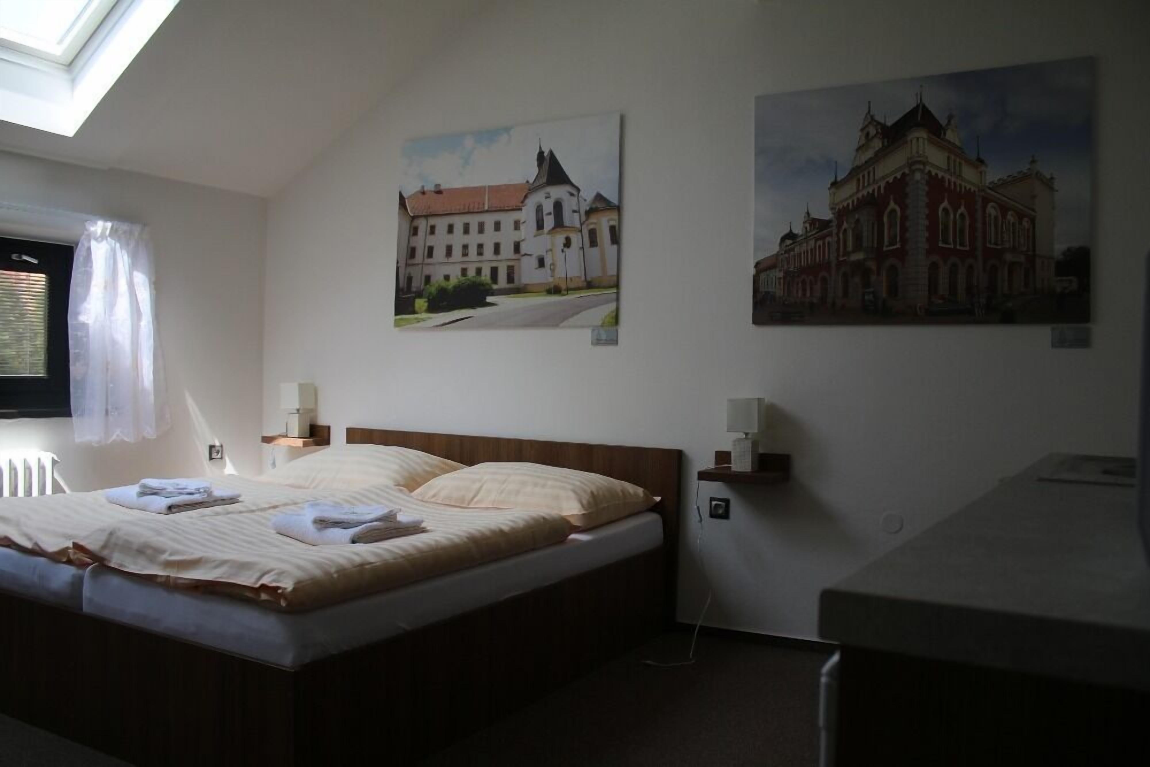 Et hotelværelse med en seng, et skrivebord og to billeder af bygninger på væggen.