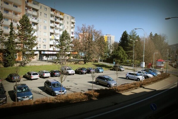 A parking lot with multiple cars, a building with balconies, and a clear sky. - Hotel Pod Radnicí (Sumperk)