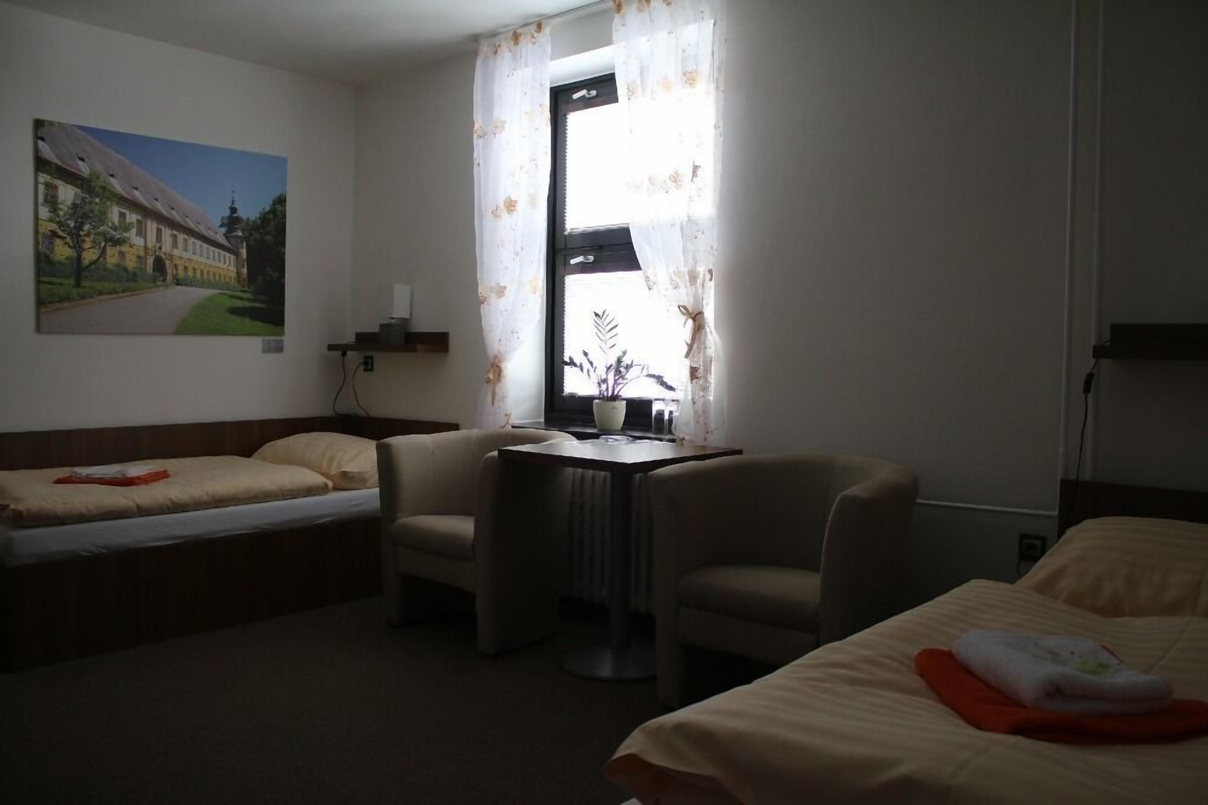 Ett hotellrum med två separata sängar, ett litet bord, en stol, ett fönster med gardiner och en tavla på väggen.