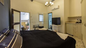 A bedroom with a bed, a television, a desk, and a kitchenette. - Mark House (Nazareth)