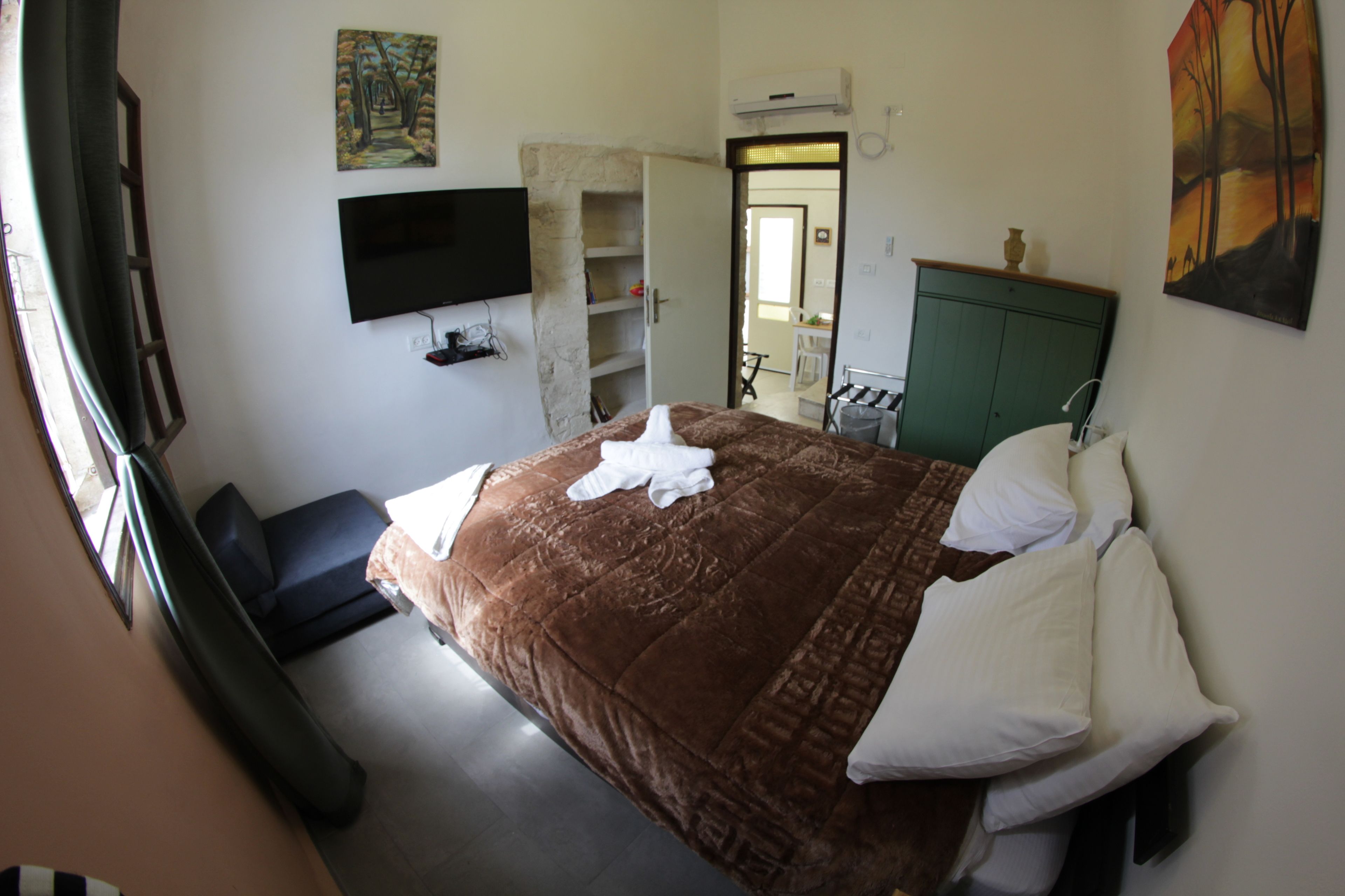 Une chambre d’hôtel avec un grand lit, un téléviseur à écran plat fixé au mur, une armoire verte et un tableau accroché au mur.
