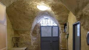 A narrow hallway with a stone wall and a tiled floor, leading to a door with a metal gate. - Mark House (Nazareth)