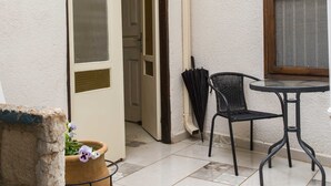 A small, enclosed outdoor area with a door leading to a room, a potted plant, a table with a chair, and a window with a blind. - Mark House (Nazareth)