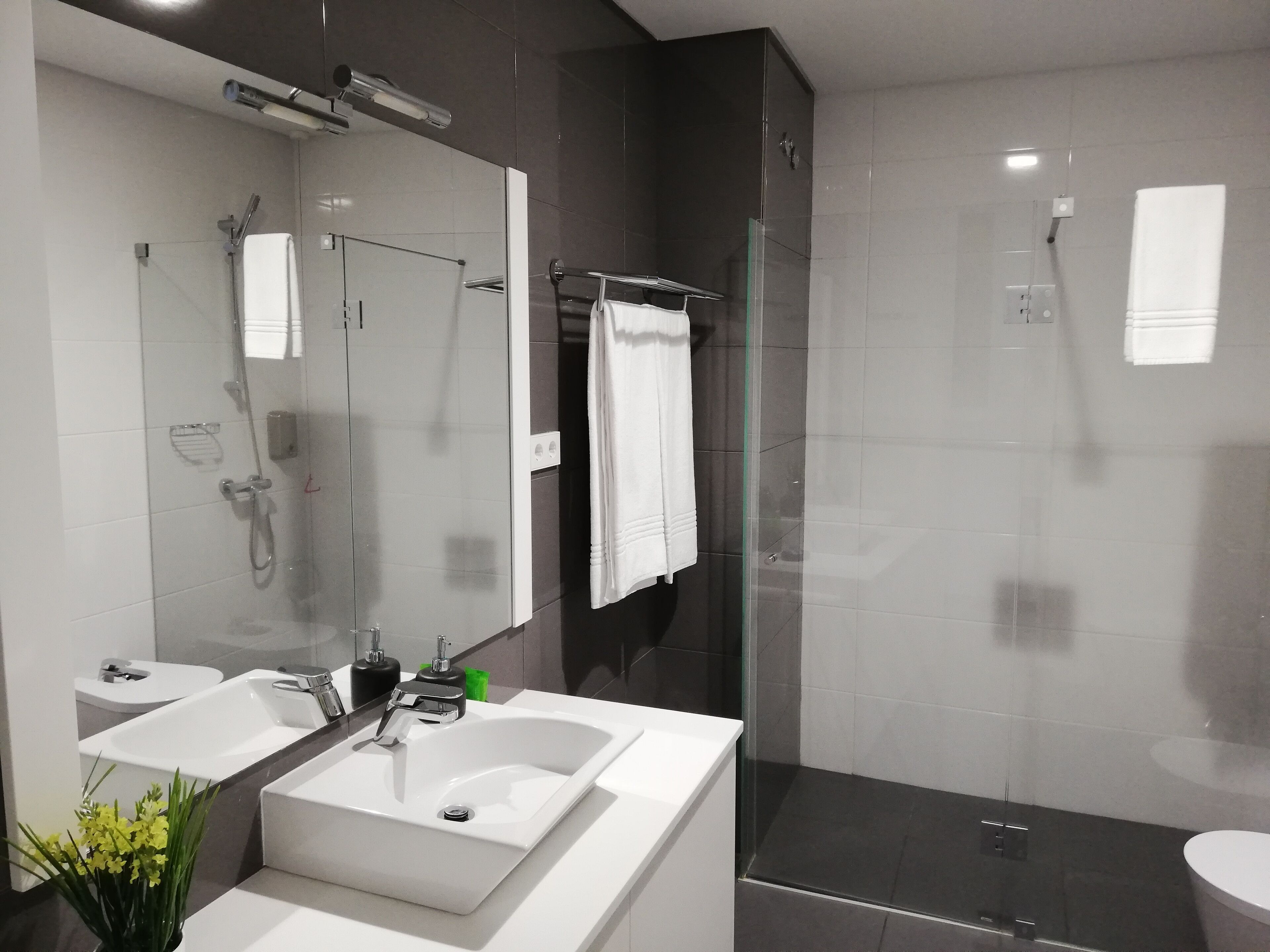 A modern bathroom with a large mirror, two sinks, a shower, and a glass-enclosed shower area.