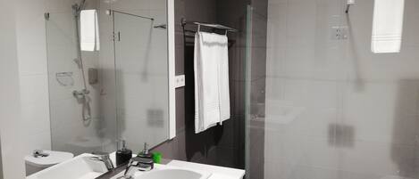 A modern bathroom with a large mirror, two sinks, a shower, and a glass-enclosed shower area.