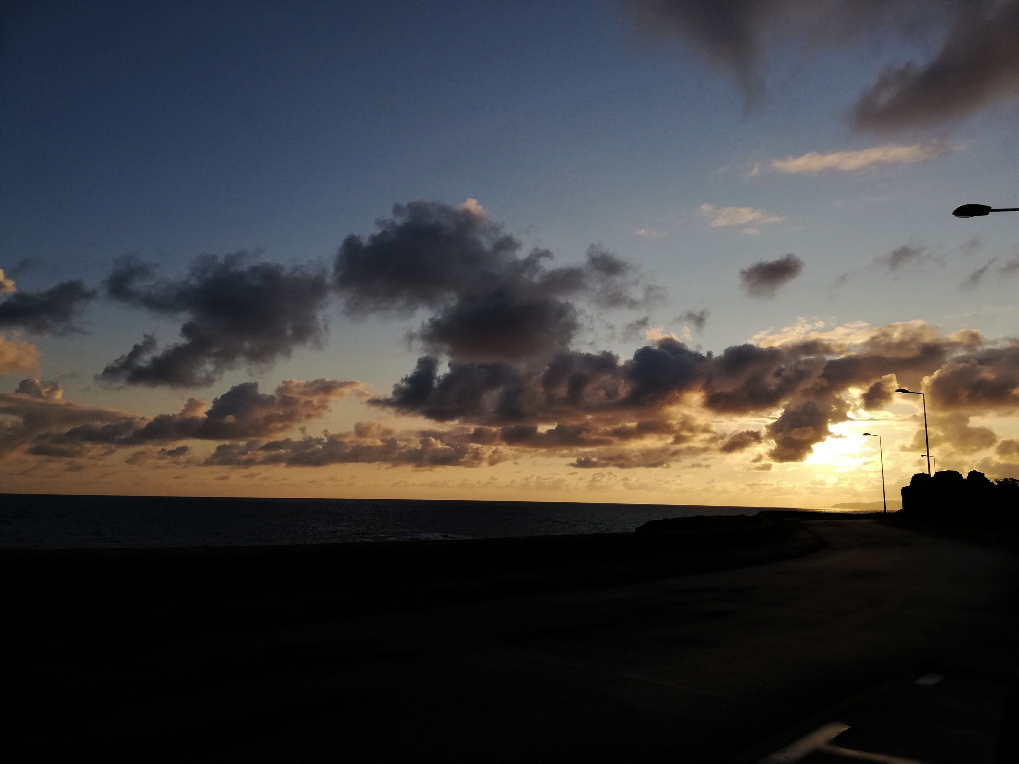 A sunset over a beach with silhouettes of street lamps and a road.