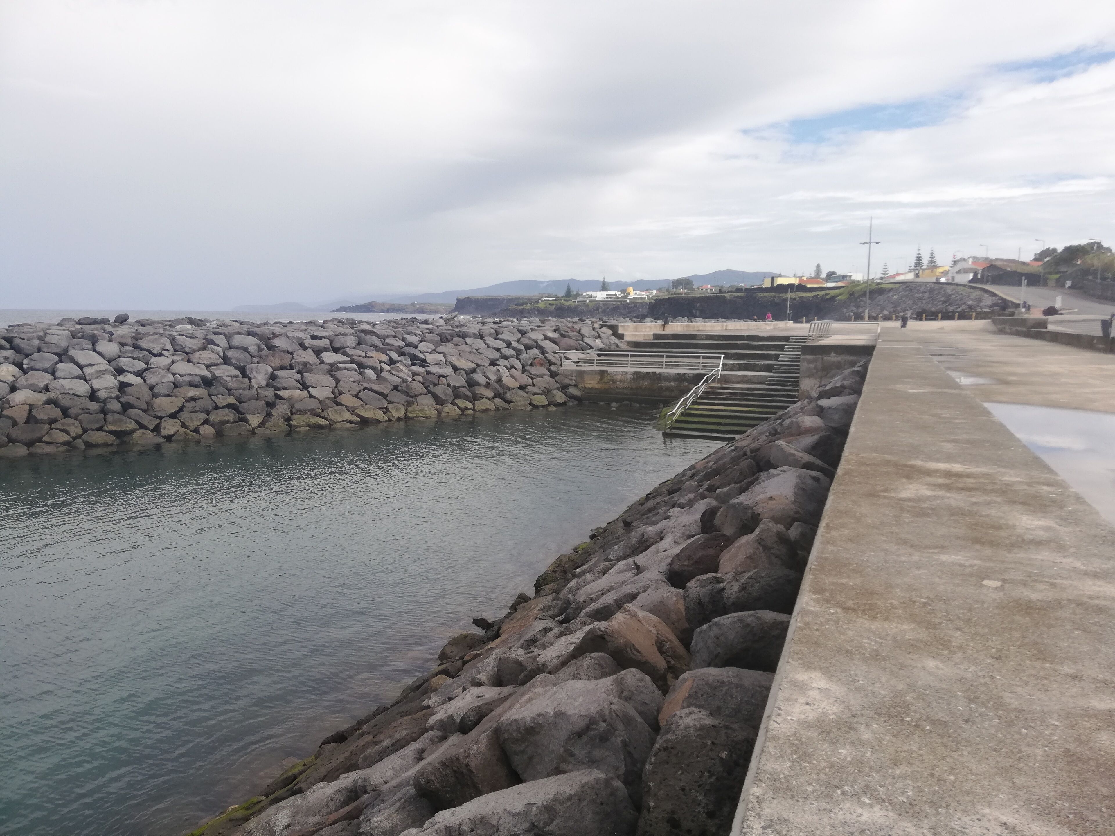 Una passeggiata costiera con un molo roccioso e un sentiero in cemento.