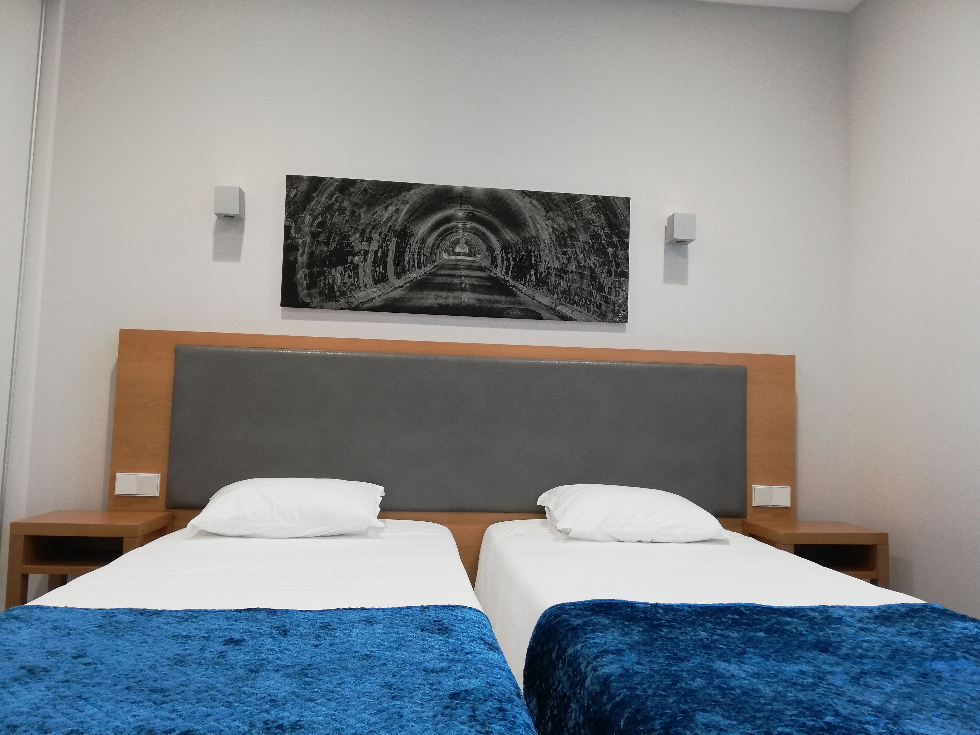 A hotel room with two beds, a large painting of a tunnel, and a wooden headboard.