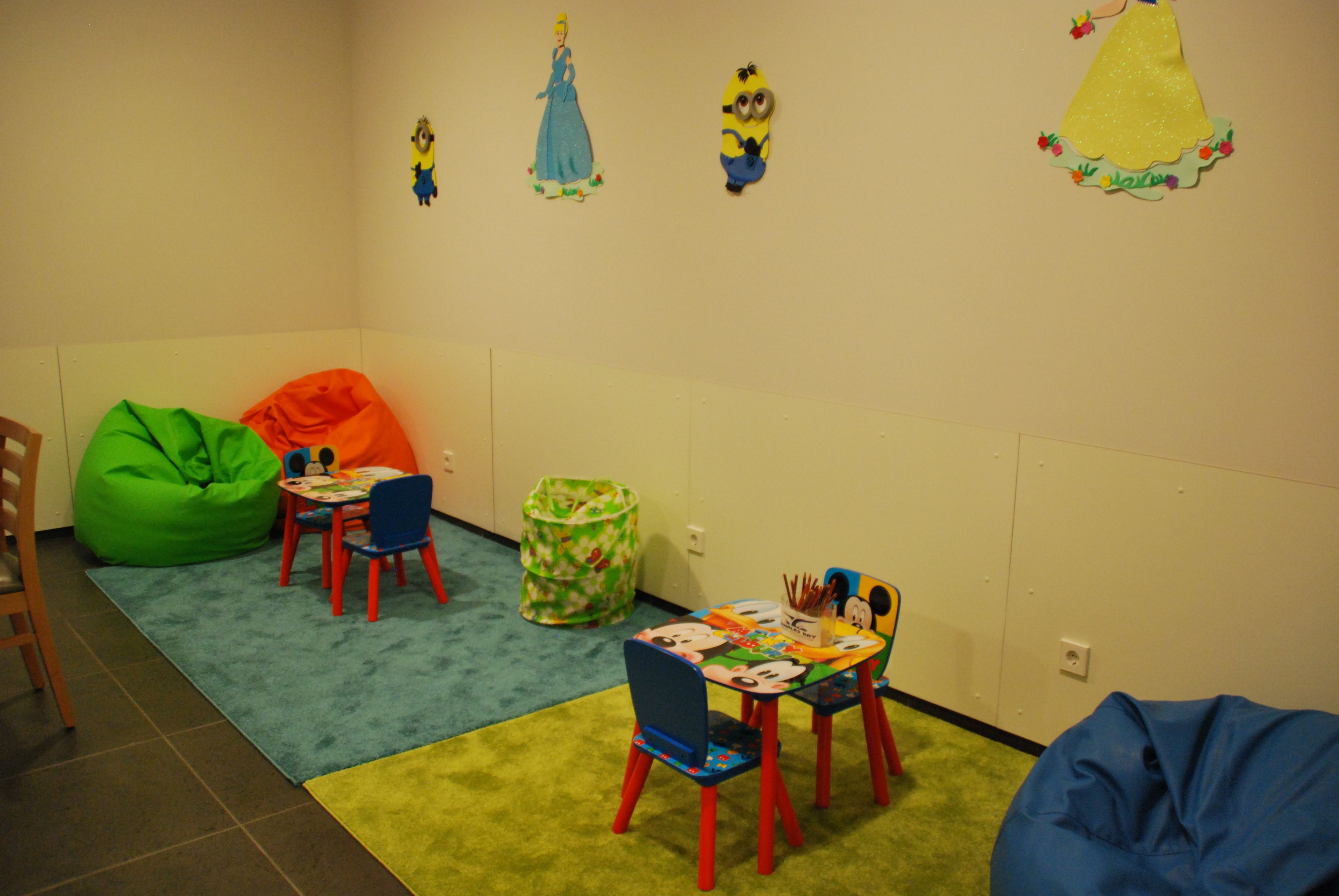 A children's playroom with colorful bean bags, a small table with a Mickey Mouse-themed tablecloth, and wall decorations including a princess and minions.