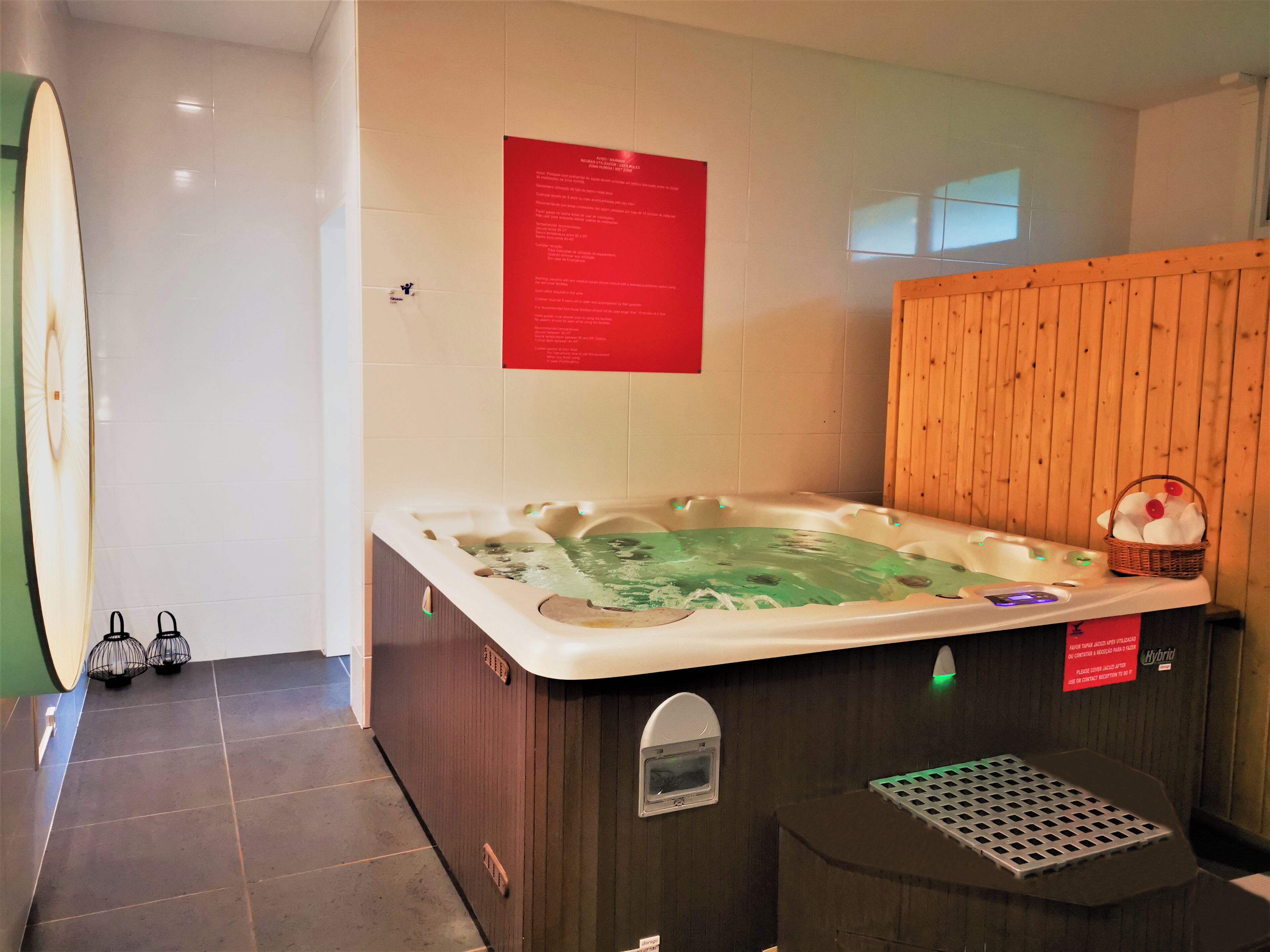 A spa room with a large hot tub, a wooden wall, and a small basket with flowers.