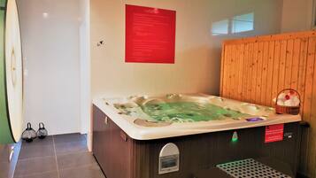 A spa room with a large hot tub, a wooden wall, and a small basket with flowers.
