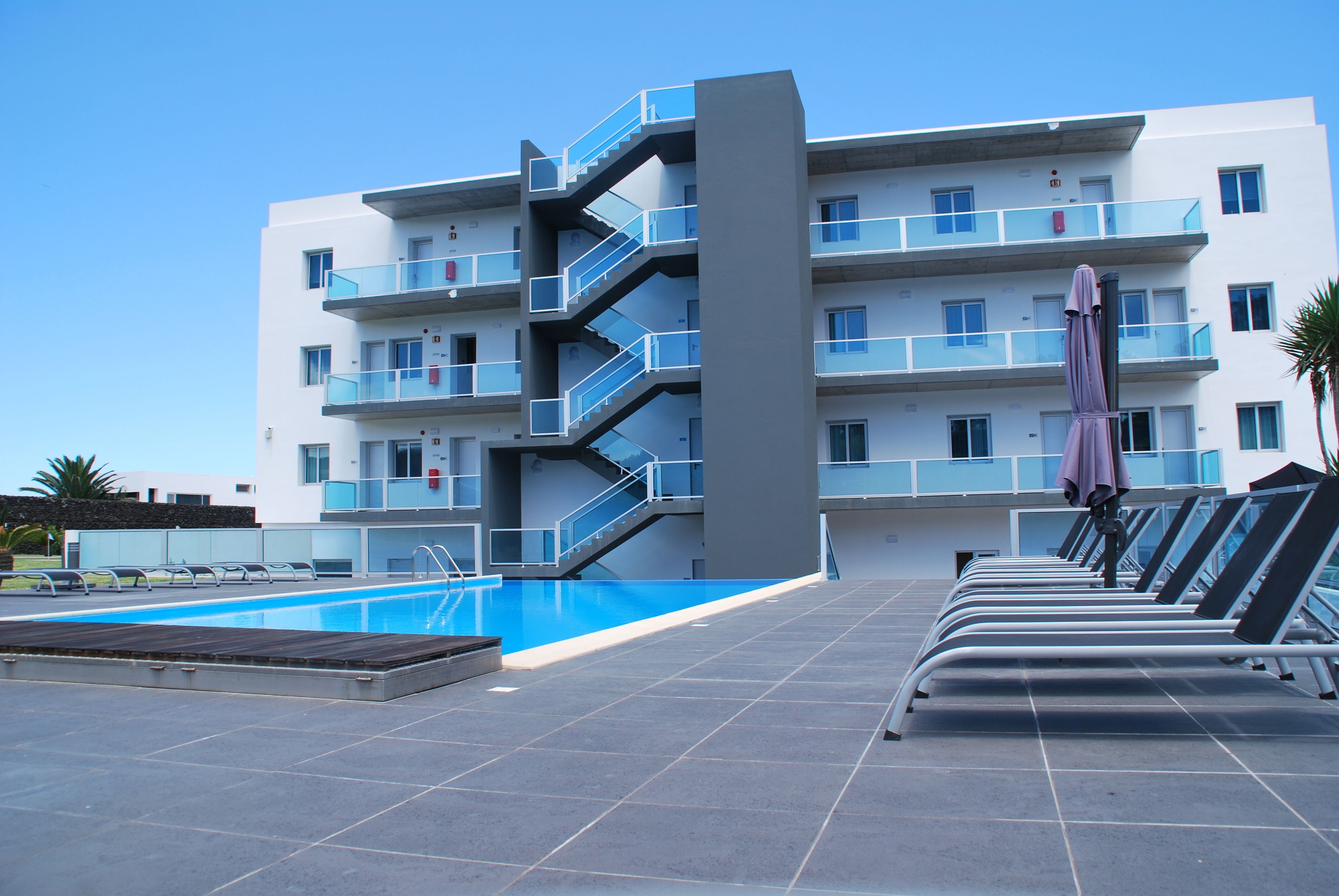 A modern building with a swimming pool and sun loungers.