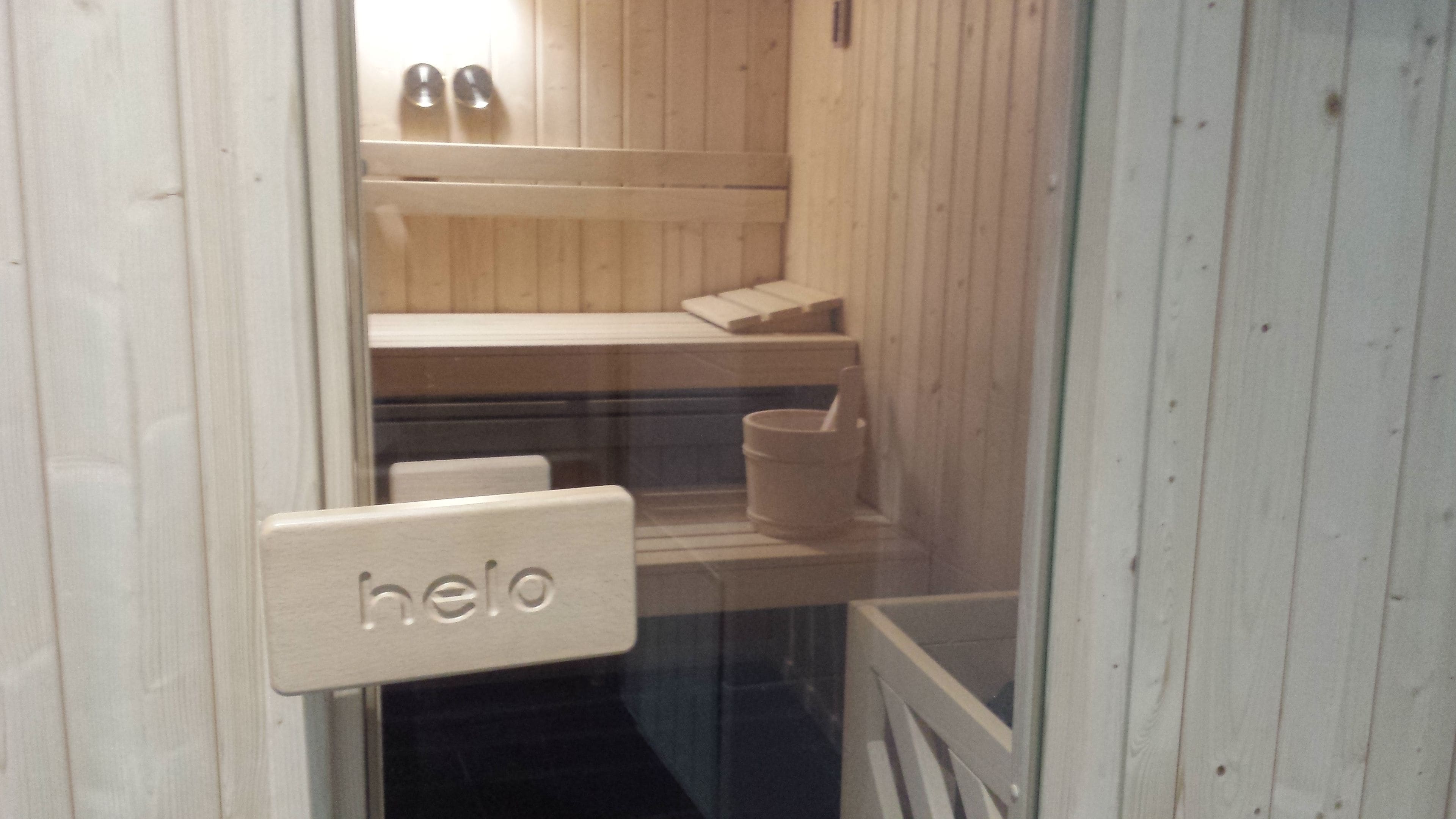 A sauna room with wooden walls, a bench, a bucket, and a 'hello' sign on the door.