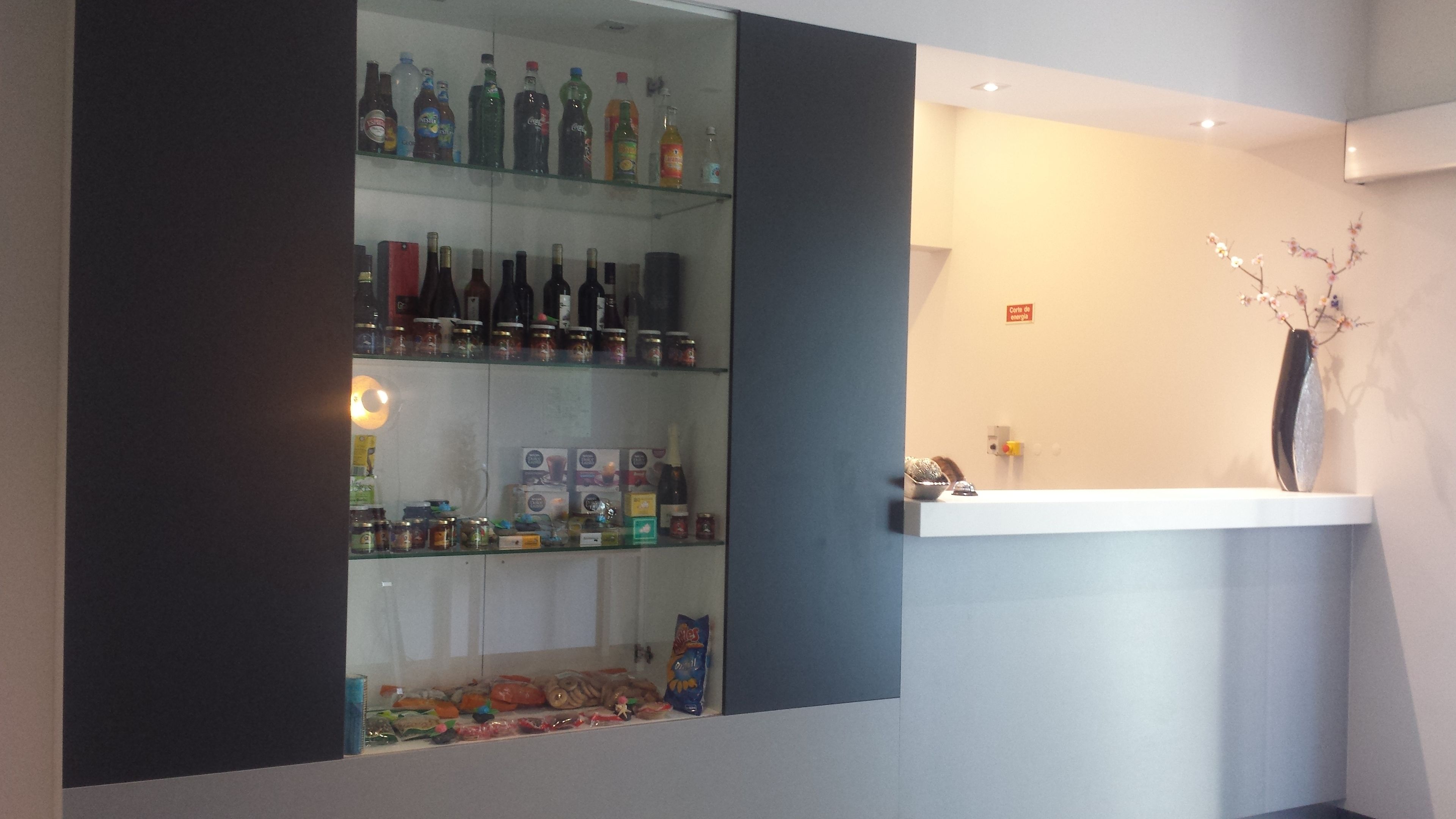 A reception area with a glass display case containing various bottles and jars, a white counter, and a vase with flowers.