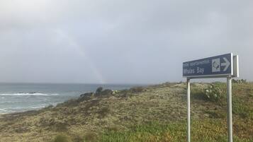 Un panneau de signalisation indiquant la direction de « hôtel-appartements » et de « Whales Bay », avec une plage et l’océan en arrière-plan.