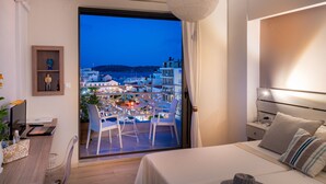 Habitación de hotel moderna con balcón que ofrece vistas a un paisaje urbano al atardecer.
