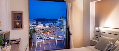 Habitación de hotel moderna con balcón que ofrece vistas a un paisaje urbano al atardecer.