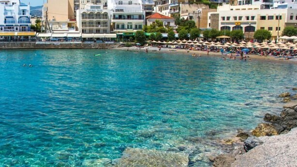 Una zona costera con aguas azul turquesa, costa rocosa y edificios al fondo.