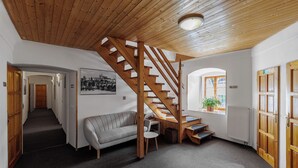 A spacious room with a wooden staircase, a grey sofa, a small table, and a potted plant. - Hotel Bella (Prague)