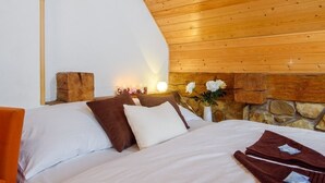 A bedroom with a wooden ceiling, a stone wall, and a bed with white and brown bedding. - Hotel Bella (Prague)