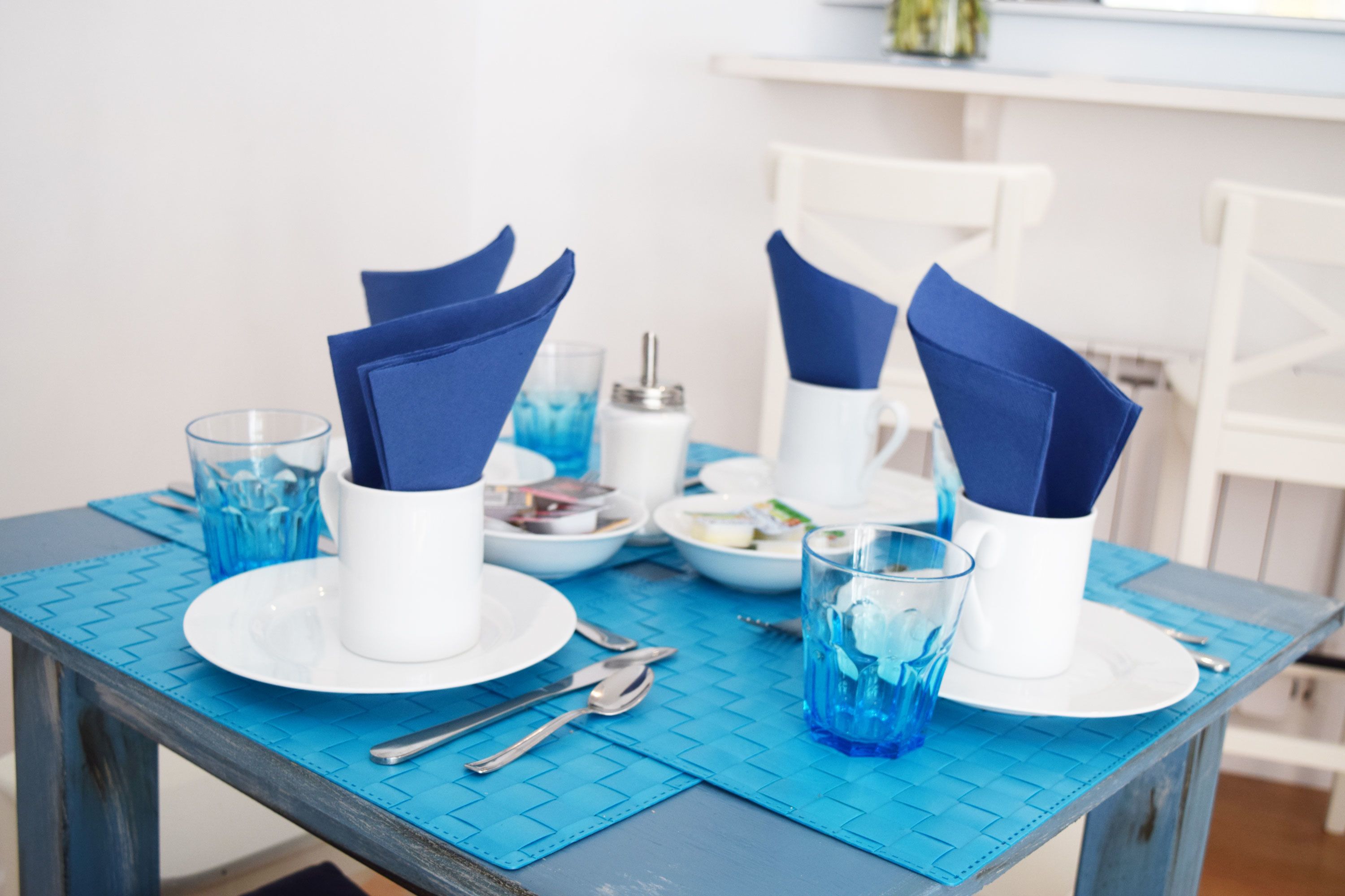 A dining table set with blue napkins, white plates, and clear glasses.