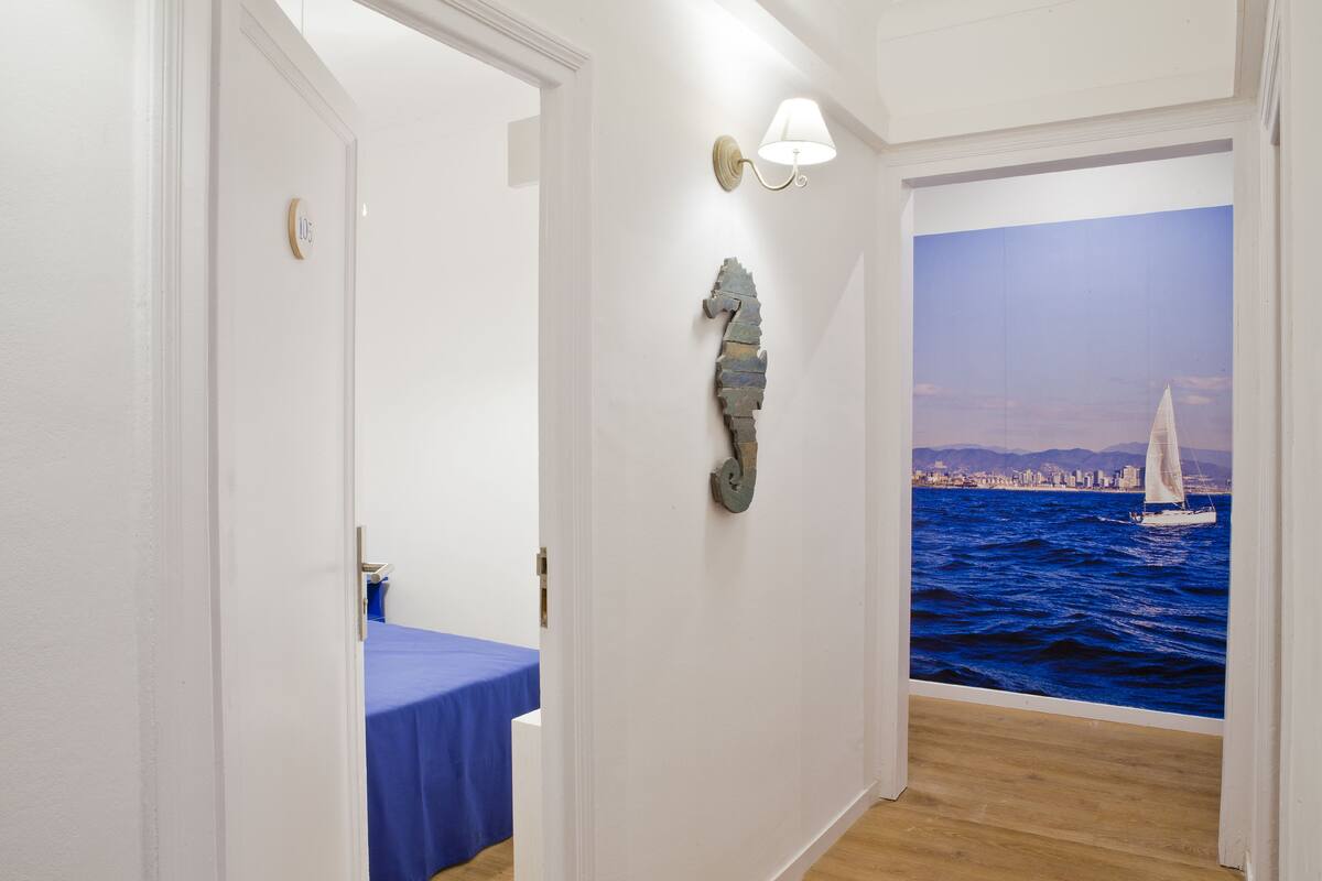 A hallway with a blue table, a wall-mounted light fixture, and a mural of a sailboat on water.
