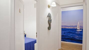 Un pasillo con una mesa azul, un aplique de pared y un mural de un velero sobre el agua.