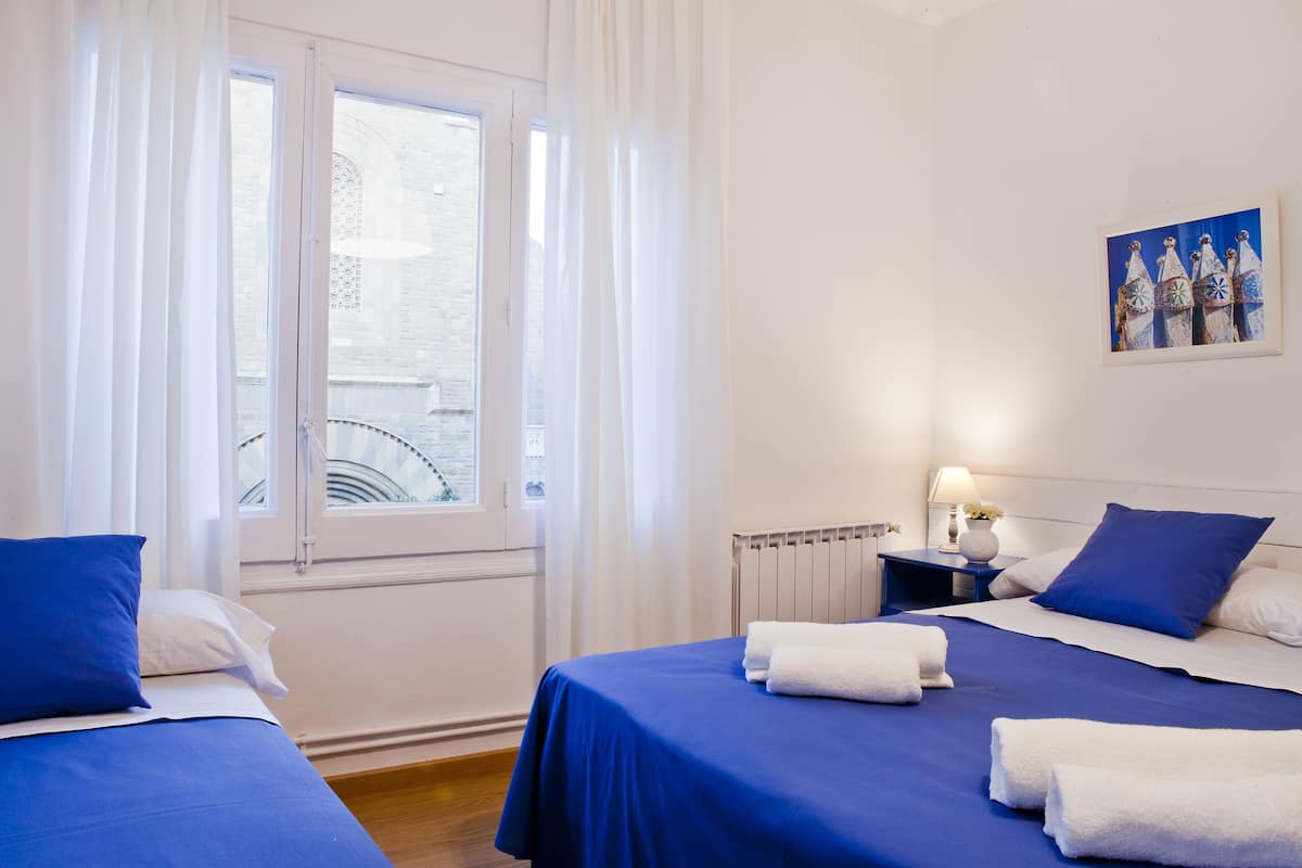 A hotel room with two beds, white walls, a window with curtains, a radiator, and a painting on the wall.