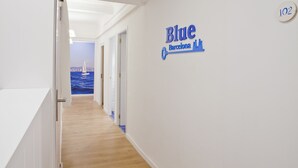 A hallway with a wooden floor leading to a room with a view of the sea. A sign on the wall reads "Blue Barcelona." - Blue Barcelona (Barcelona)