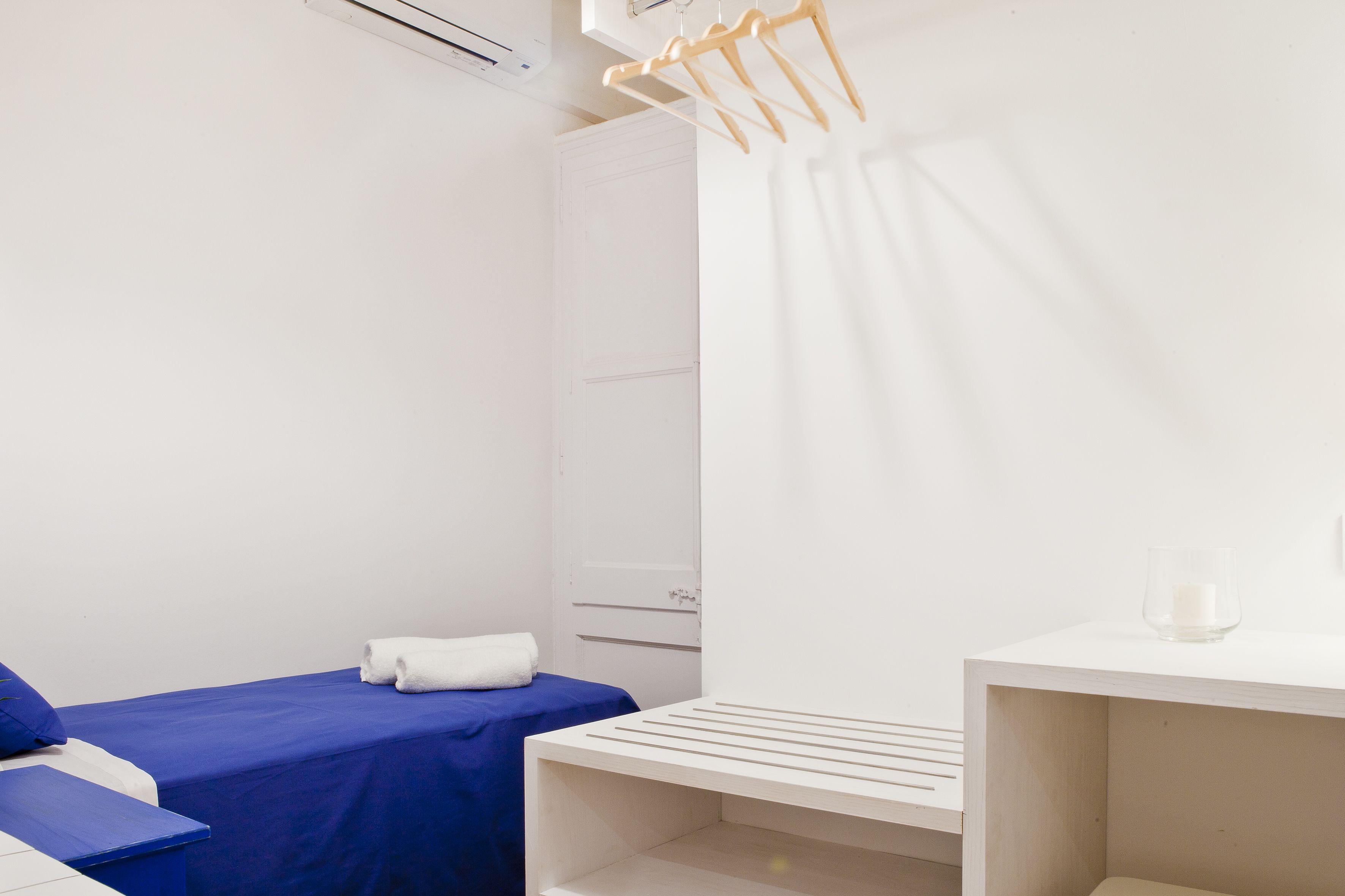 Una habitación de hotel con una cama, una mesita pequeña, un perchero y un armario blanco.