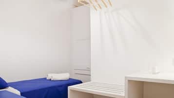 Una habitación de hotel con una cama, una mesita pequeña, un perchero y un armario blanco.