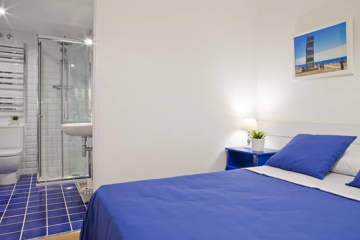 A bedroom with a bed, a nightstand, a wall-mounted picture, and a bathroom with a shower and toilet.