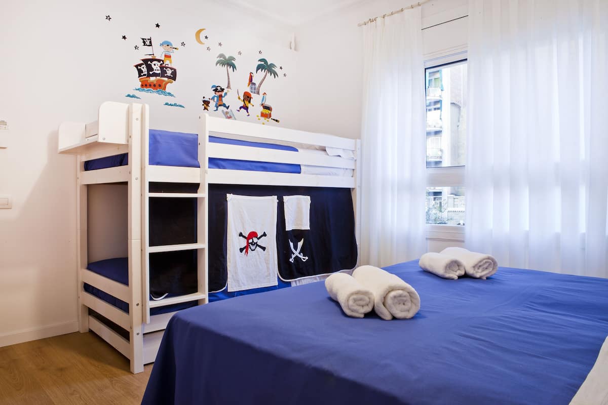 A bunk bed room with a blue bedspread, two rolled towels, and a pirate-themed wall decal.
