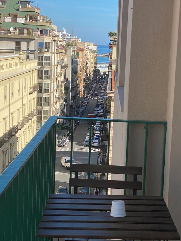 A balcony with a view of a busy street and buildings, a wooden bench, and a white cup.