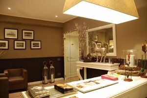 Una habitación luminosa con un espejo grande, cuadros en la pared, una mesa blanca con objetos decorativos y un sillón marrón.